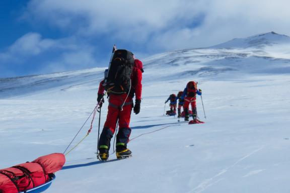 Mount Sidley climbing team sets out pulling sleds and carrying backpacks and wearing crampons.